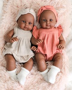 two baby dolls laying next to each other on a blanket