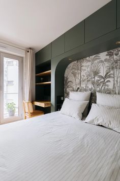 a bed with white sheets and pillows next to a window