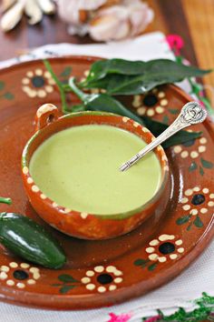 a bowl of soup on a brown plate with flowers and leaves around the bowl, next to a spoon