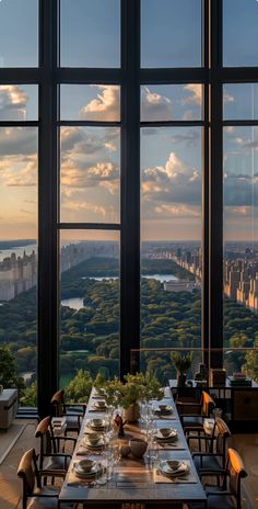 a dining room with large windows overlooking the city and surrounding trees is shown at sunset