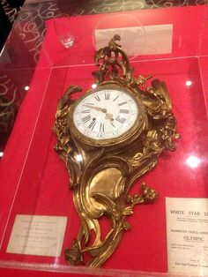 a gold clock sitting inside of a red case on display in a glass case with writing underneath it