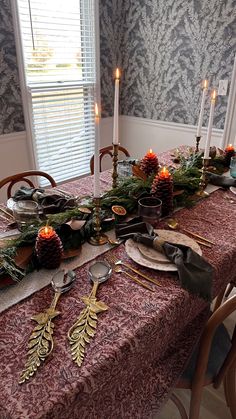 the table is set for christmas dinner with pine cones, evergreen garland and silverware