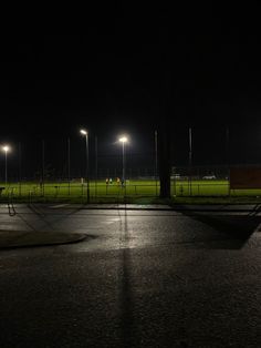 an empty parking lot at night with street lights on the grass and people walking around