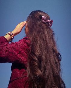 a woman with long brown hair and a pink bow on her head is looking up into the sky