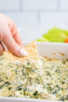 a hand dipping a tortilla chip into a white bowl filled with spinach and cheese