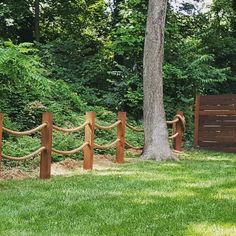 a wooden fence in the middle of a grassy area with trees and bushes behind it