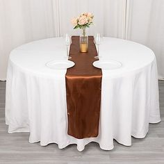 a white table topped with a vase filled with flowers next to a brown table cloth