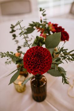 two vases filled with red flowers on top of a white tablecloth covered table