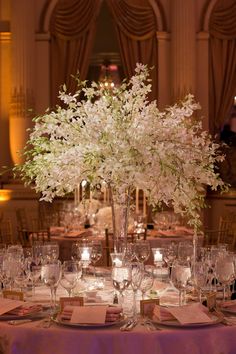 the centerpieces on this table are all white flowers and branches with candles in them