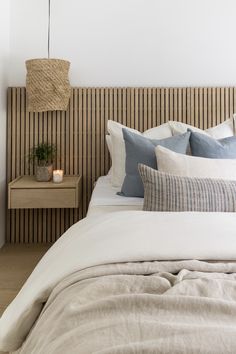 a bed with white linens and blue pillows in a neutral bedroom, next to a wooden headboard