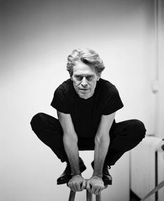 a black and white photo of a man on a stool