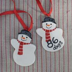 two ceramic snowmen are hanging from red ribbon