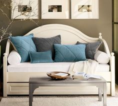 a white couch with blue and grey pillows on it in a living room area next to a coffee table