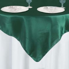 two empty wine glasses sitting on top of a green table cloth with white plates and silverware