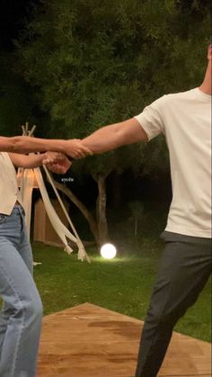 two people holding hands while standing on top of a wooden platform in front of trees