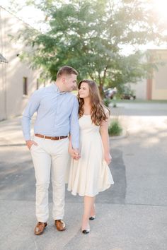 an engaged couple holding hands and walking down the street in front of a tree at sunset