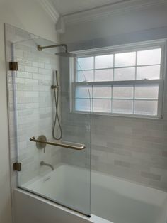 a bath tub sitting under a window next to a shower head in a bathroom with white tiles on the walls