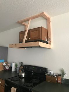 a stove top oven sitting under a wooden shelf above it's burner and microwave