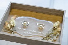 two wedding rings in a wooden box with flowers on the bottom and an inscription underneath them