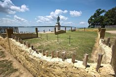 a stone wall with crosses on it and a statue in the background, near water