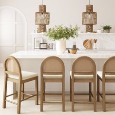 a white kitchen with marble counter tops and wooden chairs around the table, surrounded by potted plants