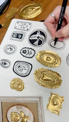 a person is drawing on paper with gold stamping and some other items in front of them