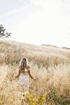 a woman walking through tall grass on a sunny day