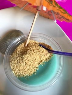 a small bowl filled with sand next to an umbrella on top of a white table