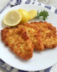 two fried fish fillets on a white plate with lemons and parsley