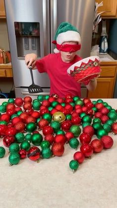 a young boy in a santa hat and red shirt is surrounded by christmas ornaments on a kitchen counter