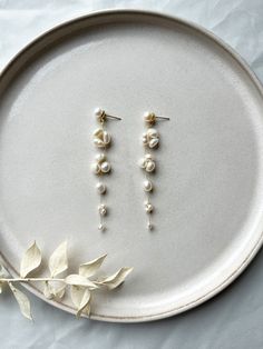 two pairs of pearl drop earrings on a white plate next to a plant with leaves