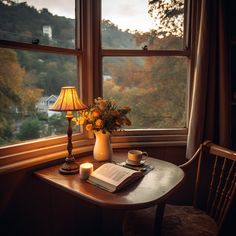 a table with a book, candle and flowers on it in front of a window