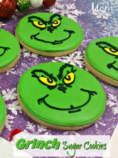 grinch sugar cookies with green frosting and yellow eyes on a purple tablecloth