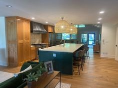 a large open kitchen and living room with wood flooring, green couches, white counter tops and wooden cabinets