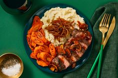 a blue plate topped with meat, potatoes and gravy next to two green forks