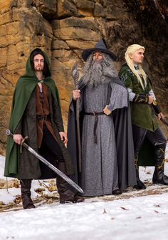 three men dressed in medieval costumes standing next to each other on snow covered ground with rocks behind them