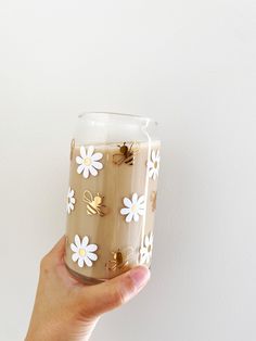 a hand holding a glass with flowers painted on the side and gold rings attached to it