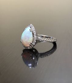 an opal and diamond ring sits on a reflective surface