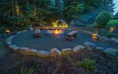 an outdoor fire pit surrounded by rocks and lights in the evening with trees around it