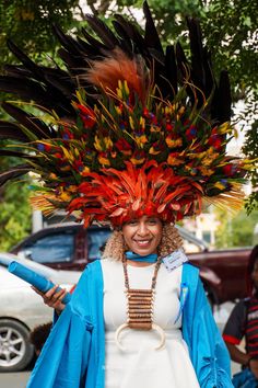 a woman wearing a colorful headdress and feathers on her head is walking down the street