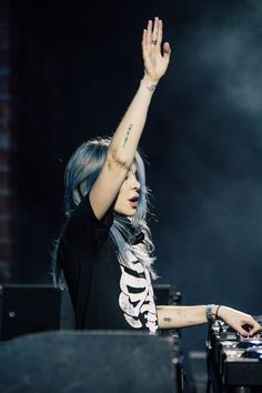 a woman with blue hair is holding her hand up in the air at a music festival