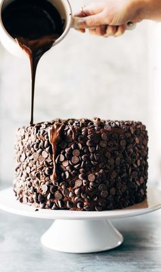 someone pouring chocolate sauce on top of a cake