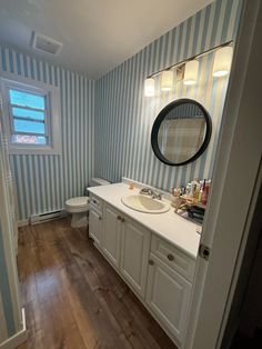 a bathroom with blue and white stripes on the walls, wood flooring and a round mirror