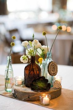 vases filled with flowers and candles sit on a wood slice at the center of a table