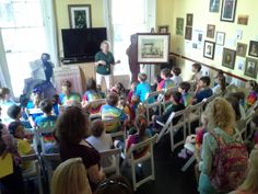 a group of children sitting in chairs watching a woman speak to them from the front row