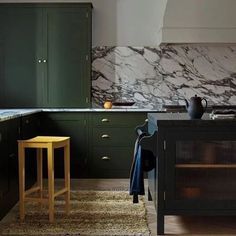 a kitchen with dark green cabinets and marble counter tops, an island in the middle