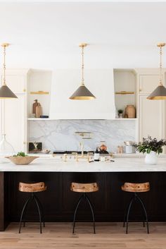 a kitchen with marble counter tops and stools in front of an island that has three lights hanging over it