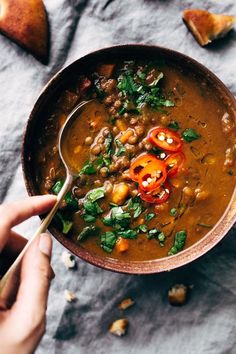 a person holding a spoon in a bowl filled with beans and vegetables on top of a table