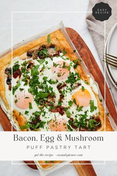 bacon, egg and mushroom puff pastry tart on a cutting board next to silverware