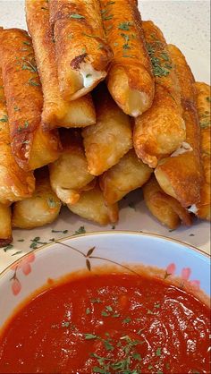 some fried food is on a plate next to a bowl of tomato sauce and dipping sauce